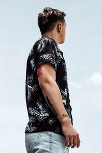 Rear view of young man with tattoos looking away against sky