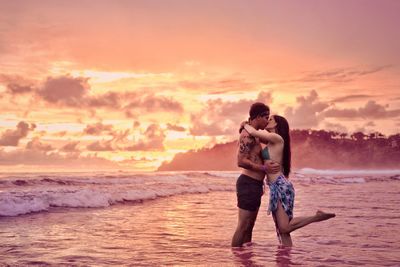 Young couple kissing on shore during sunset