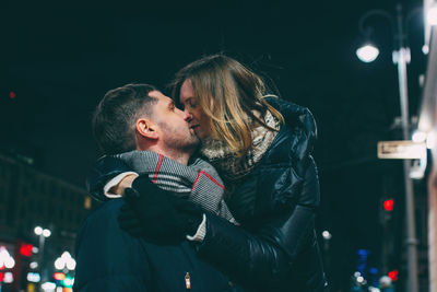 Close-up of couple kissing in illuminated city during christmas