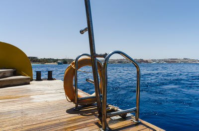 Railing by sea against clear blue sky