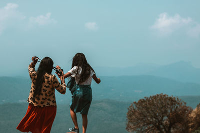 Rear view of female friends standing on cliff against sky