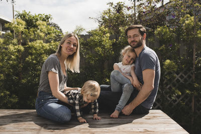 Portrait of parents and children sitting on floorboard in yard