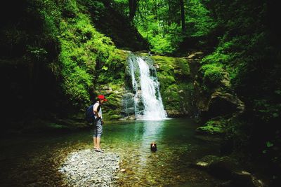 Side view of woman standing against waterfall in forest