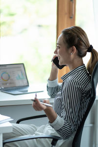 Side view of woman using mobile phone while sitting on table