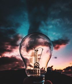 Low angle view of illuminated light bulb against sky at sunset