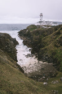 Lighthouse on beach by sea against sky