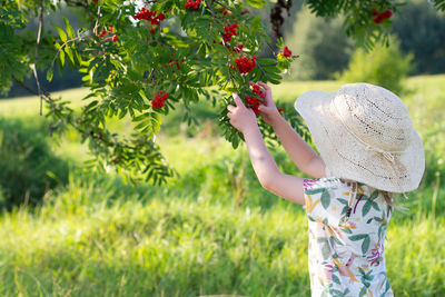 Side view of baby girl standing picking berries 