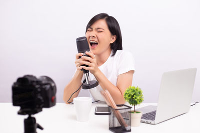 Smiling woman singing song while sitting against white background