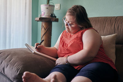 Adult woman with down syndrome studies on the sofa at home