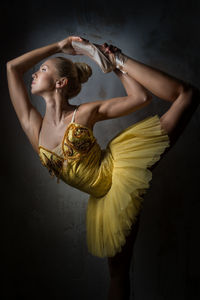 Beautiful ballerina dancing against wall in dark