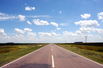 Empty road amidst field against sky