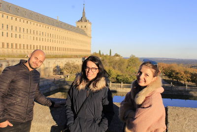 Portrait of smiling friends standing against historical palace