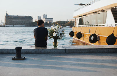 Rear view of man sitting with flowers on promenade in city
