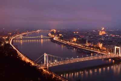 Illuminated bridge over river in city at night