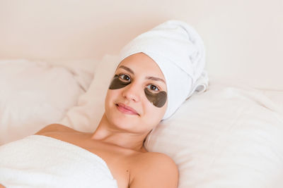 High angle view portrait of young woman with patches under eyes lying on bed at home