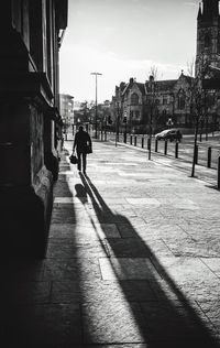 Silhouette man walking on footpath by buildings