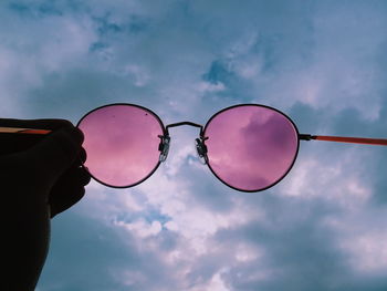 Low angle view of hand holding sunglasses against sky