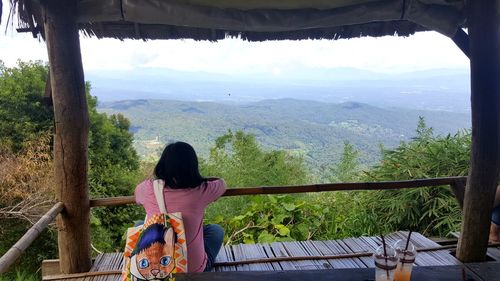 Rear view of woman sitting on railing against mountain