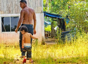 Full length of shirtless man standing by tree