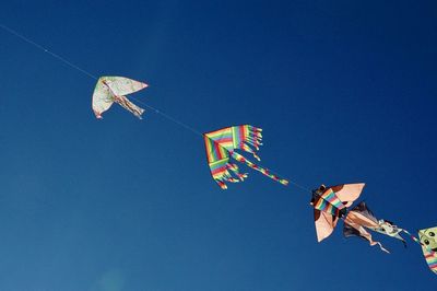 Low angle view of kites flying against clear blue sky