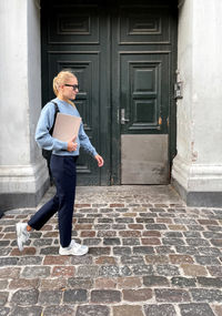 Woman wearing sunglasses going to work holding magazine against the green wall and the city