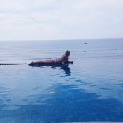 Side view of woman lying on poolside against sea and sky