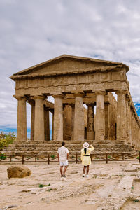 Rear view of tourists at historical building against cloudy sky