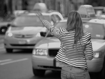 Rear view of woman stopping car while standing on street in city