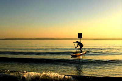 Silhouette man in sea against sky during sunset