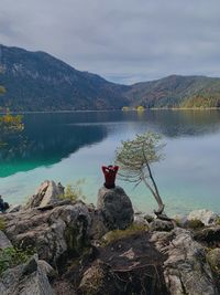 Man sitting on rock by lake against sky