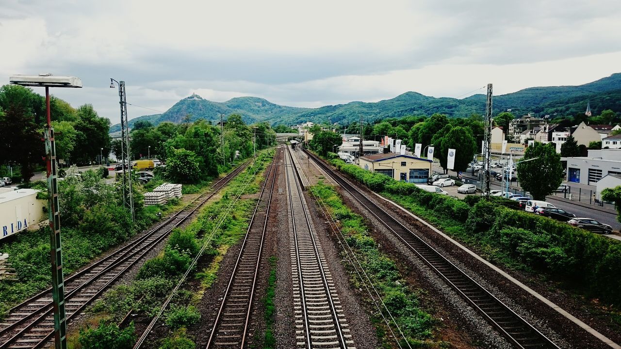 the way forward, mountain, sky, building exterior, transportation, built structure, architecture, railroad track, vanishing point, diminishing perspective, high angle view, tree, house, cloud - sky, rail transportation, road, town, power line, electricity pylon, mountain range