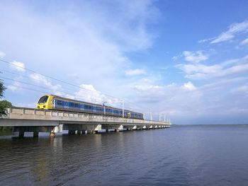 Train on bridge over sea against blue sky