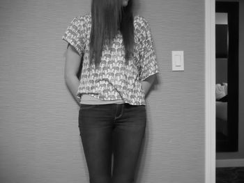 Midsection of woman standing against wall at home