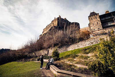 Friends in park with edinburgh castle in background against cloudy sky