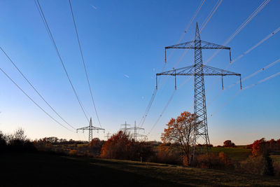 Low angle view of electricity pylon on field against clear sky