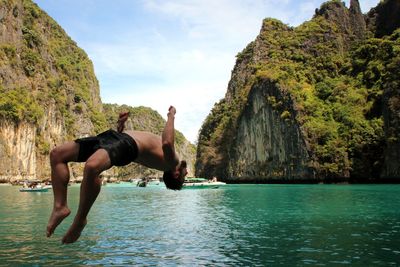 Man standing on rock by sea against sky