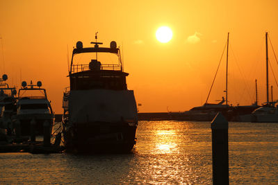 Silhouette ship sailing on sea against orange sky