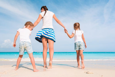 Rear view of friends enjoying at beach against sky