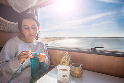 Woman knitting fabric while having coffee in train