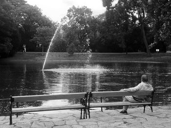 Woman sitting on bench in park by lake