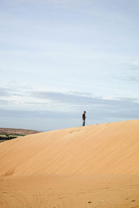 Man standing on sand dune in desert against sky