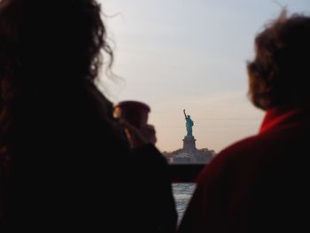 Rear view of statue in city at sunset