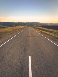 Road amidst field against sky during sunset