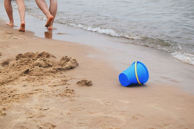 Low section of people walking by blue bucket on shore at beach