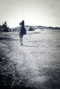 Rear view of woman walking on field against clear sky