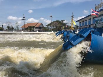 Water flowing over sea by houses against sky