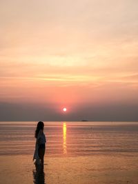 Side view of woman standing on shore against sky during sunset