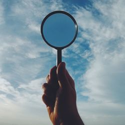 Cropped image of man holding magnifying glass against sky