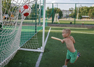 Full length of shirtless boy playing soccer on grass