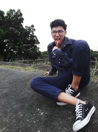 Portrait of young man sitting on road against sky